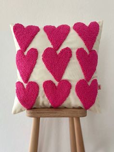 a pink and white heart pillow on top of a wooden stand next to a white wall