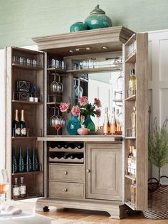 a wooden cabinet filled with lots of bottles and glasses next to a vase full of flowers