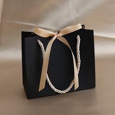 a black shopping bag with a white ribbon tied around the front and side, on a beige background