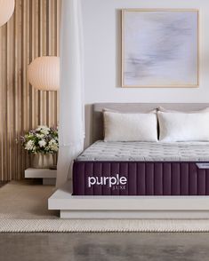 the purple mattress is on display in front of a white wall and beige striped curtains