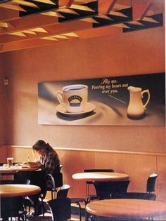 a woman sitting at a table in front of a coffee cup and saucer on the wall