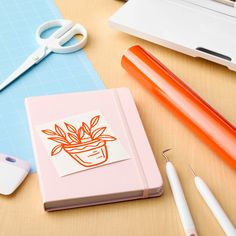 a notebook with a plant on it sitting next to some pens and paper cutters