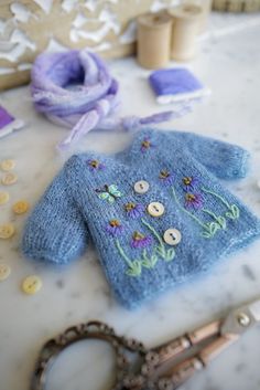 a blue sweater with flowers on it next to some scissors and other crafting supplies