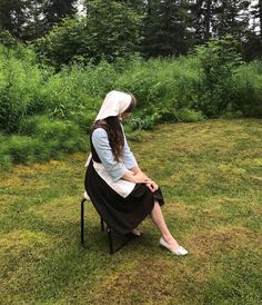 a woman sitting on top of a chair in the middle of a grass covered field