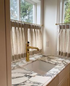 a kitchen with marble counter tops and gold faucet in front of the window