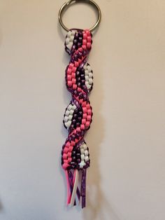 a pink, white and black keychain hanging from a metal hook on a wall