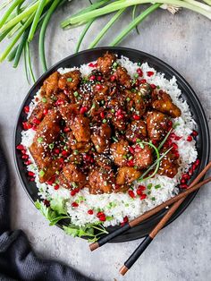 a black plate topped with rice and meat covered in sesame seeds next to chopsticks