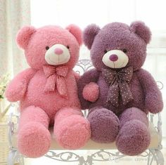 two teddy bears are sitting on a bench with pink and purple fur, one is wearing a bow