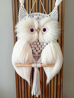 an owl made out of white yarn and feathers on a wooden wall hanging from a wood slat