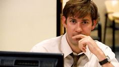 a man sitting in front of a computer monitor with his hand on his chin and looking at the screen