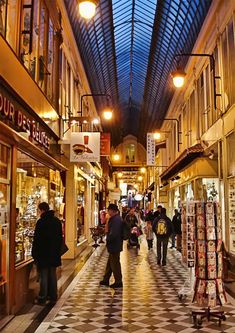 people are walking through an indoor shopping mall with many stores on the sides and ceiling lights above them