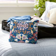 an open bag sitting on top of a bed next to a pillow and purse with clothes in it