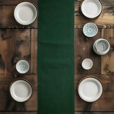 the table is set with white dishes and green placemats on wood planks