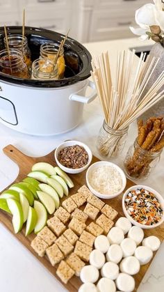 an assortment of snacks are arranged on a cutting board next to a crock pot