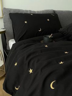 a black comforter with gold stars and moon designs on it, next to a night stand