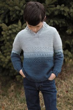 a man standing in front of some trees wearing a blue and grey sweater with an ombreed pattern