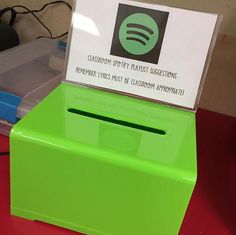 a green box sitting on top of a red table next to a plastic container with a sign