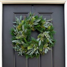 a wreath on the front door of a house decorated with greenery and white berries