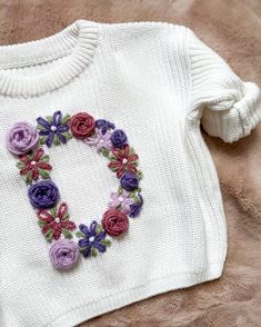 a knitted sweater with flowers on the front and back, sitting on a fur surface