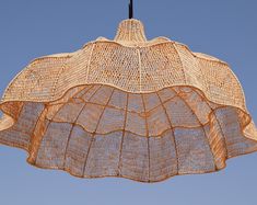 an umbrella made out of woven material hanging from a hook on a wire with a blue sky in the background