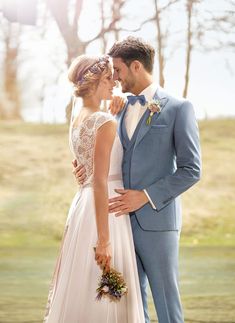 a bride and groom standing together in front of a lake wearing blue suit and bow tie