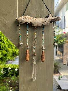 a piece of driftwood hanging on the side of a building with beaded necklaces