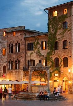 people are sitting on benches in front of an old stone building at night with umbrellas