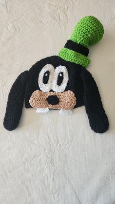 a crocheted black dog with a green hat on it's head laying on a bed