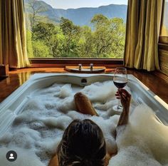 a woman sitting in a bathtub with a glass of wine next to her feet