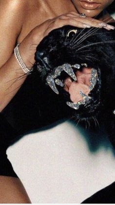 a woman holding a black cat with her hands on it's face and wearing jewelry