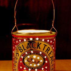 a red and gold tin can with white lights on it sitting on a wooden table