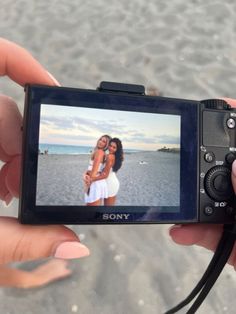 a person holding up a camera to take a photo on the beach with two women