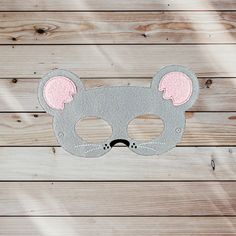 a gray mask with pink ears on top of a wooden table next to wood planks