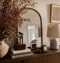 a living room with a mirror, lamp and vase on top of a wooden dresser