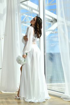 a woman standing in front of a window wearing a white dress