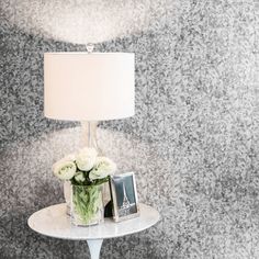 a table with a lamp and flowers on it in front of a wallpapered background