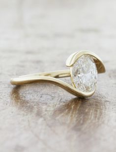 a gold ring with a white diamond on it sitting on a wooden table next to a pair of scissors