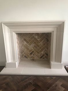 a white fireplace with wood flooring in the middle and a herringbone pattern on the mantle