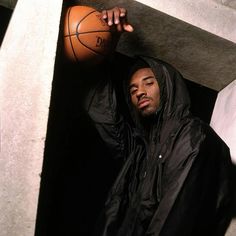 a man leaning against a wall with a basketball in his hand and wearing a black jacket