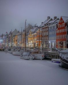 many boats are docked in the water near buildings and snow covered ground with lights on them