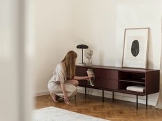 a woman kneeling down on the floor next to a table with a vase and bookshelf