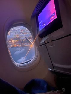 an airplane window looking out at the city lights and clouds from inside another plane's cabin