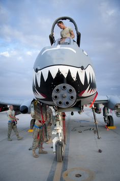 two men standing next to an airplane with a shark face painted on the front and side