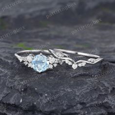 an engagement ring with blue topazte and white diamonds on a rocky surface in front of