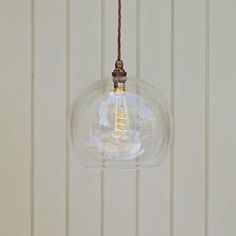 a clear glass light fixture hanging from a brown cord on a white wall with wooden planks