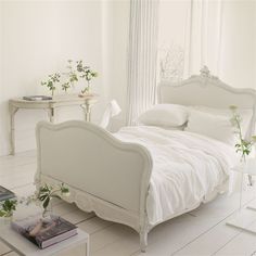 a white bed sitting in a bedroom next to a table with flowers on top of it