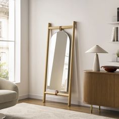 a large mirror sitting on top of a wooden stand in a living room next to a window