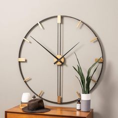 a clock that is on the wall next to a dresser with a hat and potted plant