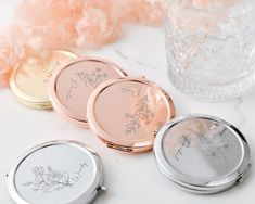 three compact mirrors sitting on top of a table next to some pink and white flowers