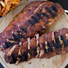 two pieces of meat on a wooden plate next to french fries